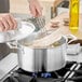 A person cooking food in a Vigor stainless steel sauce pot.