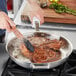 A person using a Vigor SS3 Series stainless steel fry pan to cook a piece of meat.