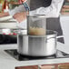 A woman cooking food in a Vigor stainless steel stock pot on a stove.