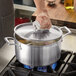 A person using a towel to remove a Vigor stainless steel lid from a pot of food.