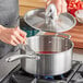 A person using a Vigor SS3 Series stainless steel saucepan with a whisk to stir liquid.