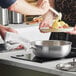 A person using a Vigor stainless steel saucier pan to cook food on a stove.