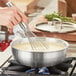 A person using a whisk to stir liquid in a Vigor Tri-Ply Stainless Steel Saucier Pan.