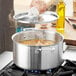 A person using a Vigor stainless steel stock pot to cook soup on the stove.