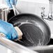 A person in blue gloves cleaning a Vigor stainless steel non-stick fry pan with a brush.