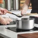 A woman and man cooking food in a Vigor stainless steel sauce pan on a stove.