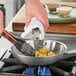 A person cooking food in a Vigor stainless steel fry pan on a stove.