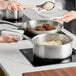 A woman uses a Vigor stainless steel sauce pan to cook rice and meat.