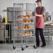 A man in a red apron standing next to a Regency wire sheet pan rack with food.