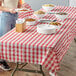 A woman standing next to a table with red and white gingham table covers with bowls of food on it.