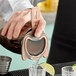 A person using a Barfly copper mesh strainer to pour a cocktail.