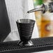 A bartender using a Barfly black measuring jigger to pour liquid.