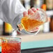 A hand pouring liquid from a Barfly Retro Design Glass Bitters Bottle into a drink.