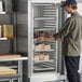 A man taking a tray of cakes from a Regency end load sheet pan rack in a refrigerator.