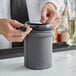 A person using a Barfly gray protective sleeve to hold a mixing glass on a counter.