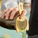 A person using a Barfly gold fine mesh spring strainer to pour green liquid into a glass.