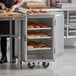 A woman wearing gloves loading pastries onto a Regency sheet pan rack.