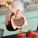 A person using a Barfly copper spring bar strainer to pour a red cocktail into a glass.