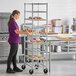 A woman in a kitchen with a Regency side load platter rack holding trays of bread.