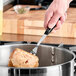 A hand holding a Vollrath stainless steel pot fork with a black handle over a pot of meat.