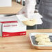 A person in gloves using Choice interfolded bakery tissue to line a tray of food.