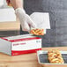 A person wearing gloves putting pastries into a box using Choice interfolded bakery tissue.