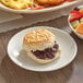 A Bakery Chef buttermilk biscuit with jam on a plate next to a bowl of fruit.