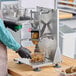 A person in a blue shirt and black gloves uses a Garde heavy-duty French fry cutter on a countertop.