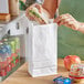 A person putting a sandwich in a white paper bag.