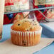 An Otis Spunkmeyer wild blueberry muffin in a paper wrapper on a blue tray.