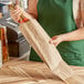 A woman holding a Choice natural kraft paper bag in front of a counter with a bottle inside.