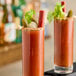 Two glasses of Zing Zang Bloody Mary next to a bottle of Zing Zang Bloody Mary Mix on a bar table.