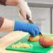 A person wearing blue Ansell knitted gloves peeling a mango.