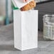A hand putting food into a white Choice paper bag with handles.