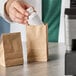 A person putting a white bottle into a natural brown Kraft paper bag on a counter.