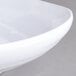 A close-up of a white Carlisle square melamine plate with a curved edge.