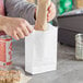 A person opening a Choice white paper bag to reveal a plastic container of pretzels.