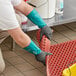 A man wearing Ansell AlphaTec dishwashing gloves cleaning a red floor with a plastic mat.