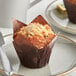 An Otis Spunkmeyer blueberry crumb cake muffin in a brown wrapper with a crumb topping on a plate.