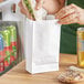 A person putting a sandwich in a white paper bag.