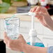 A person using a Lotus Plant Energy syrup pump to pour blue liquid into a glass of ice.