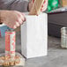 A person opening a white paper bag to reveal a plastic container of food.