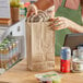 A woman holding a sandwich in a Choice natural Kraft paper bag.