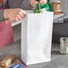 A man pouring beer from a green bottle into a white paper bag.