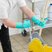 A man wearing green Ansell AlphaTec Solvex gloves and using a mop to clean a floor.