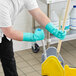 A man wearing green Ansell AlphaTec Solvex gloves using a mop to clean a floor.