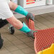 A person wearing Ansell AlphaTec dishwashing gloves with black and green rubber gloves holding a black rubber mat.