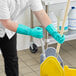 A man in green Ansell Solvex gloves mopping a school kitchen.