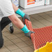 A person wearing green and gray Ansell gloves holds a red plastic mat.