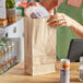 A woman putting food in a Choice natural kraft paper bag on a counter.